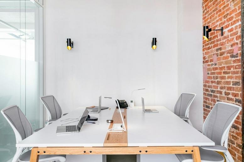 Spacious meeting room at 33 Rue Truffaut featuring a long white table, grey chairs, and a red brick accent wall.