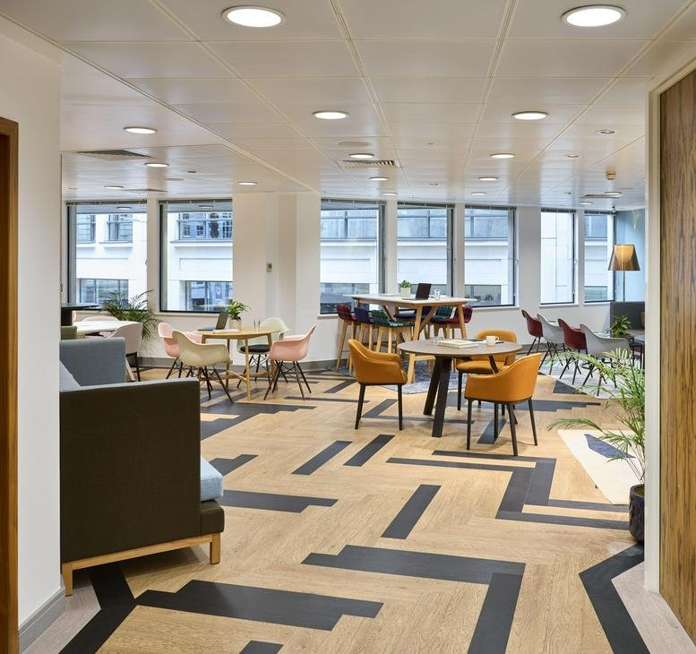 Bright breakout space with patterned flooring and colorful mid-century modern chairs.