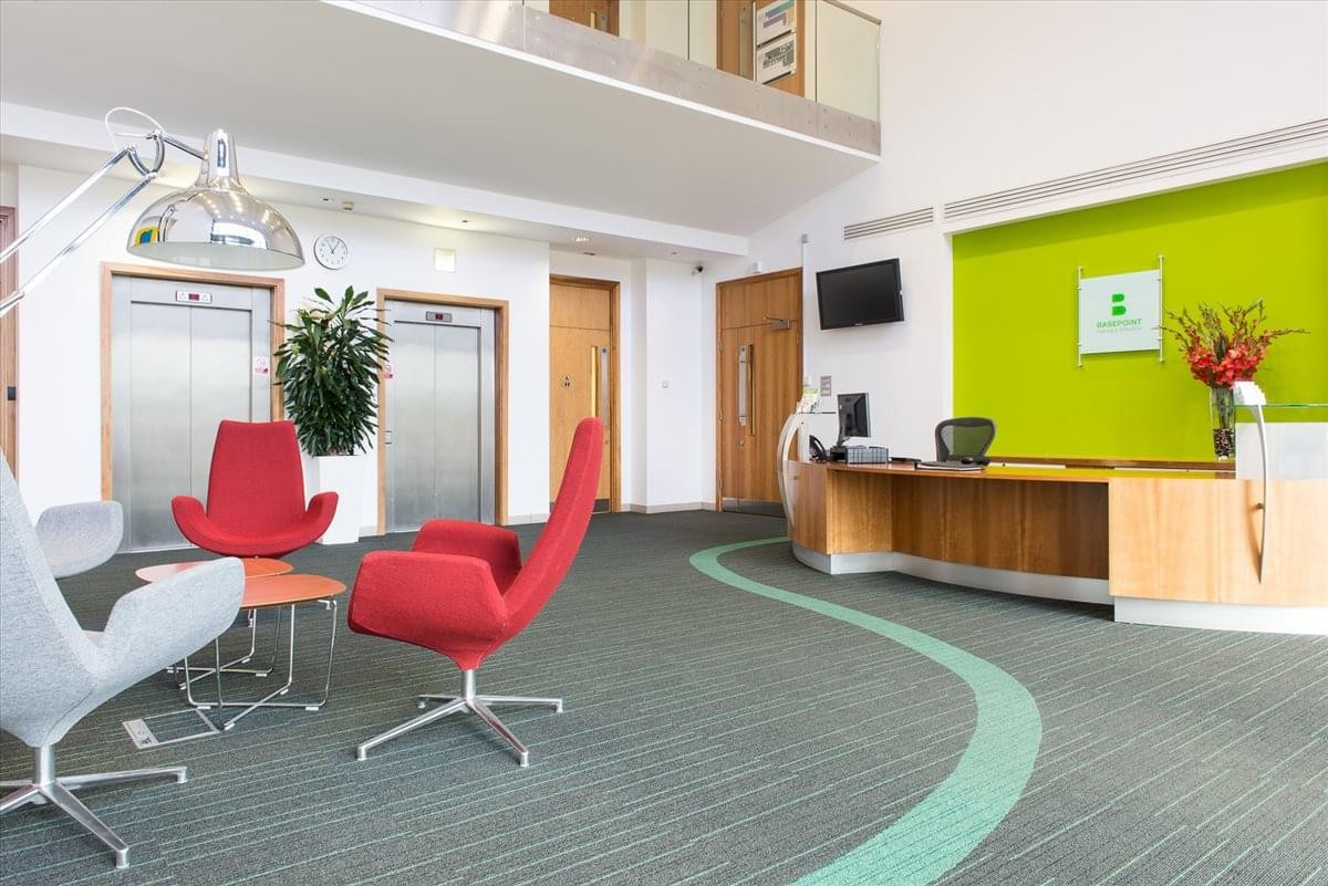Spacious reception area with a curved wooden desk, lime green feature wall, and red armchairs.