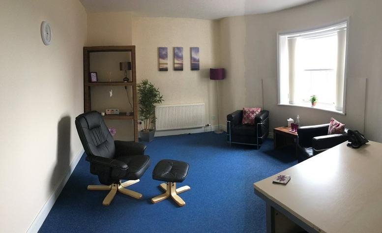 Lounge area with blue carpet, leather armchairs, and a large bay window.
