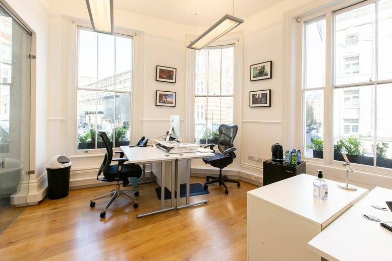 Bright workspace featuring multiple desks, wood flooring, and tall windows.