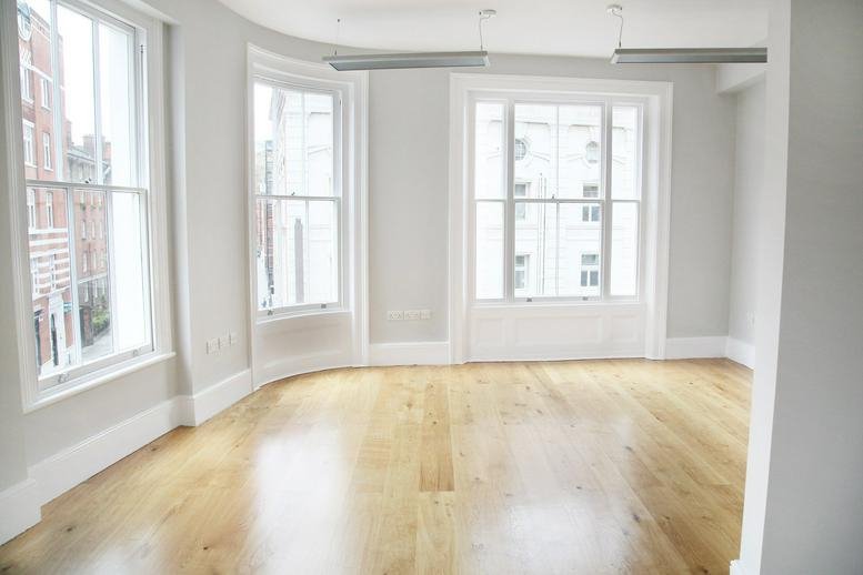 Spacious empty office room with polished wooden floors and large curved windows.