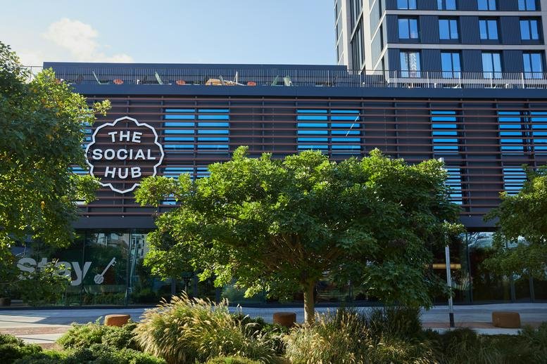 Exterior view of The Social Hub Barcelona featuring a modern facade with dark slats and green trees.