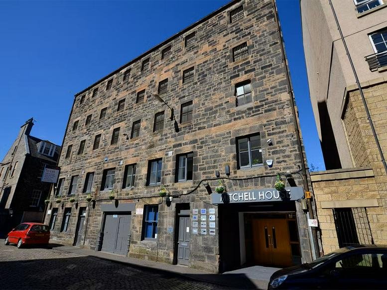 Wide-angle street view of the multi-story stone building exterior under a clear blue sky.