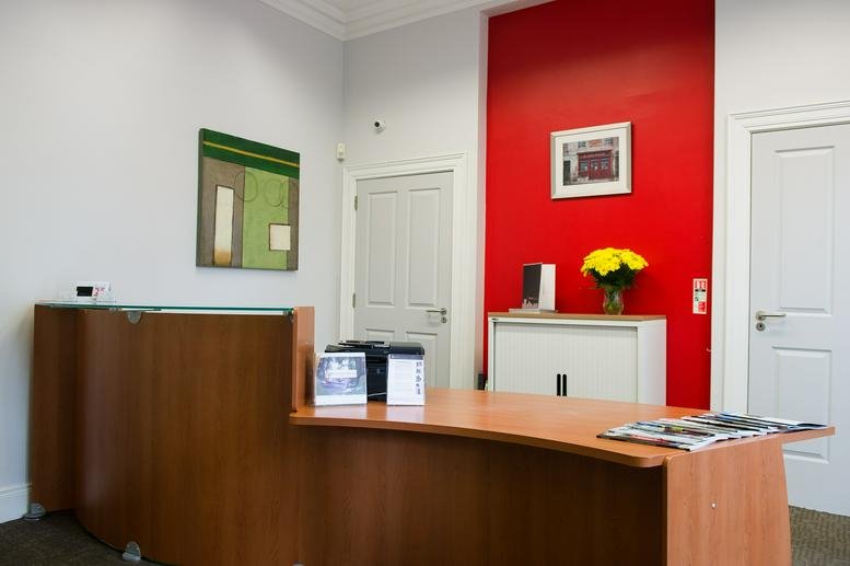 Wood-paneled reception desk at 54 Elmwood Ave with a vibrant red accent wall and yellow flowers.