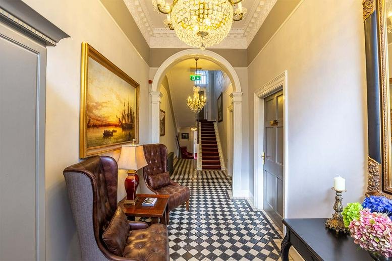 Grand entrance hallway at 56 Fitzwilliam Sqaure, Dublin, Ireland featuring a chandelier and checkerboard flooring.