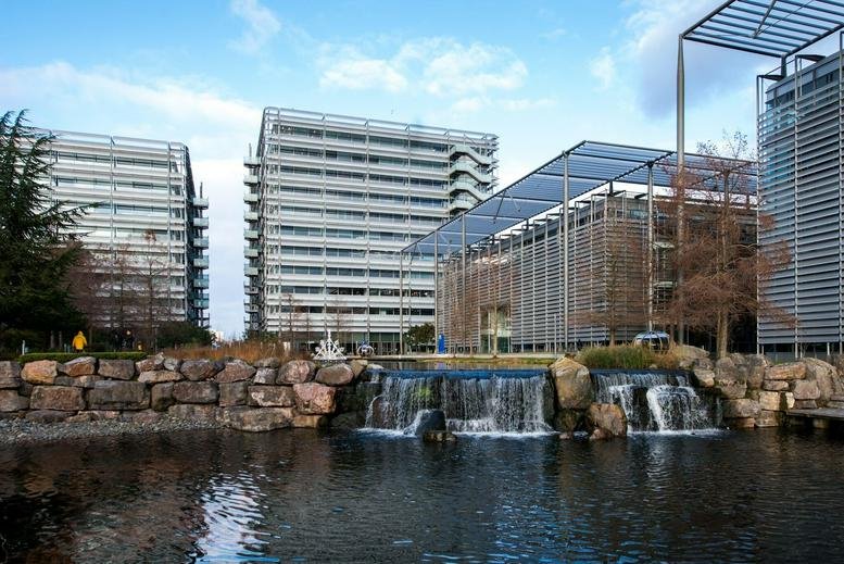 Exterior view of the modern glass facade at Building 7, Chiswick Park with a scenic lake and waterfall.