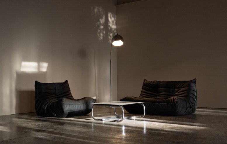 Moodily lit lounge with two low black sofas and a chrome floor lamp.