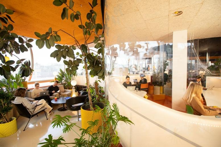 Spacious communal lounge with curved glass walls and lush potted plants at 68 Hanbury Street.