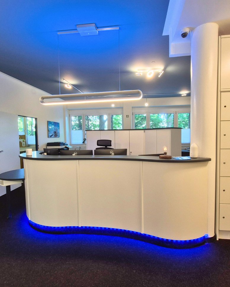 Curved white reception desk at Business Location Munich featuring vibrant blue floor lighting.