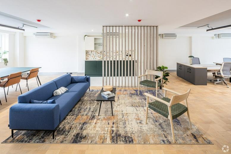 Spacious communal lounge at 74-76 Saint John Street with a blue sofa, textured rug, and wooden slat divider.