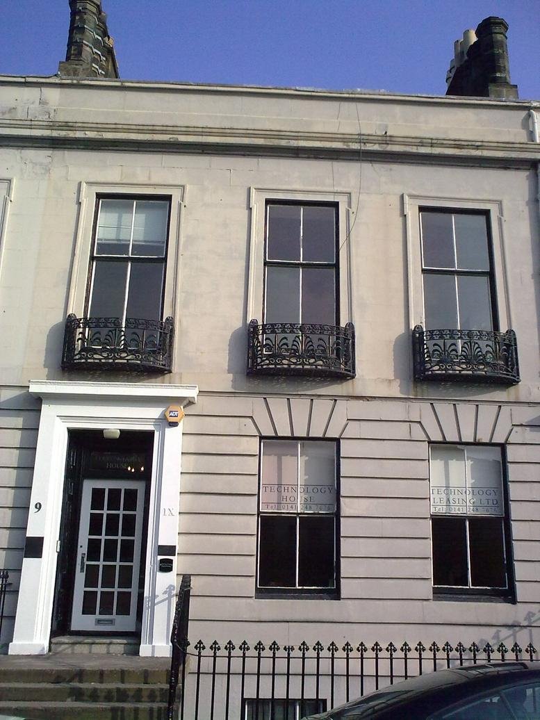 Full exterior view of the traditional stone facade featuring large windows with ornate iron railings.