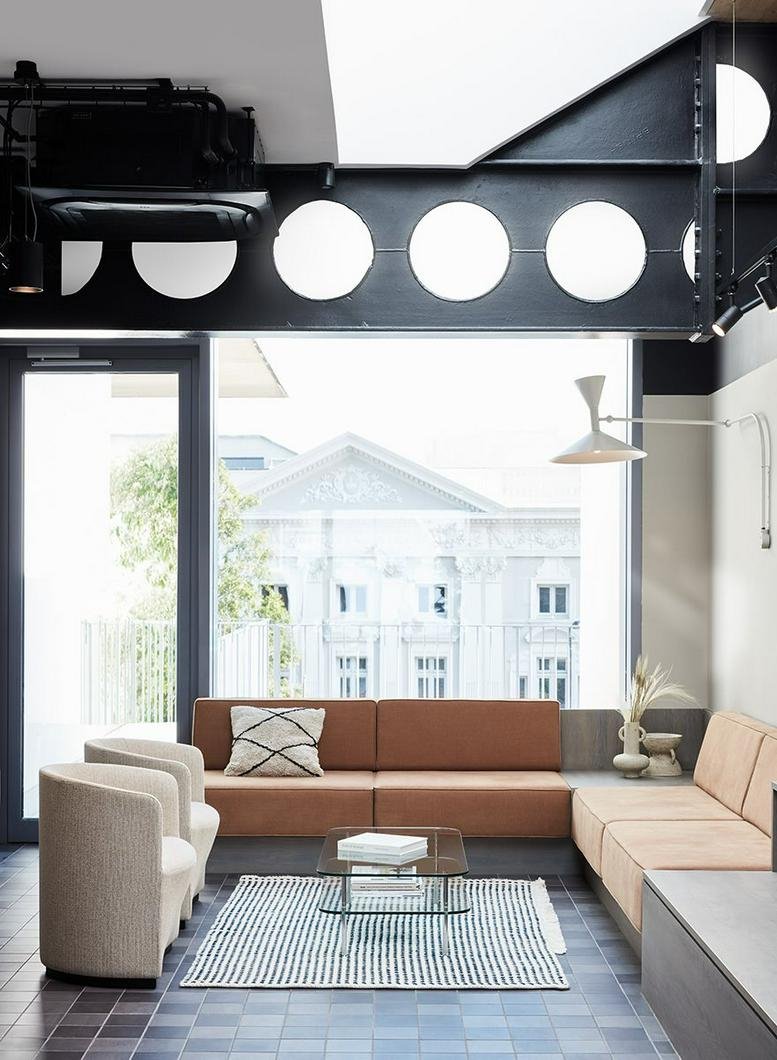 Bright communal lounge with terracotta sofas, a blue tiled floor, and views of historic buildings.