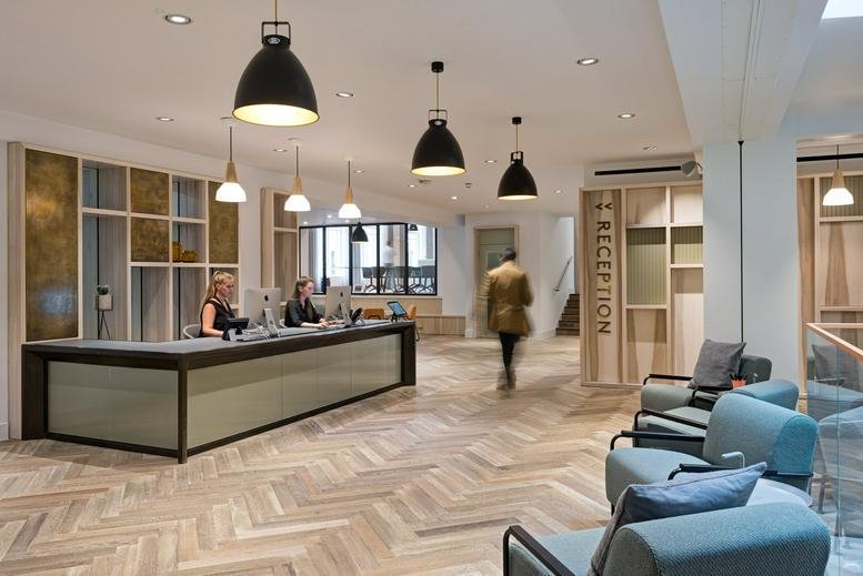 Spacious reception area with a long front desk, herringbone wood flooring, and industrial pendant lighting.