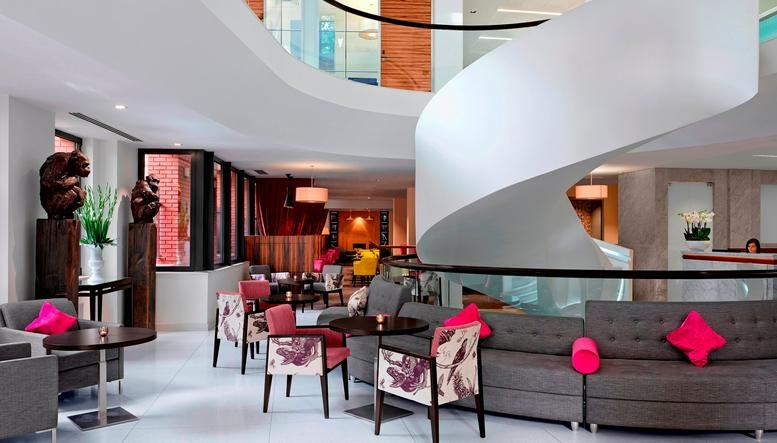 Spacious lobby at 96 Kensington High Street featuring a white spiral staircase and lounge seating with pink pillows.