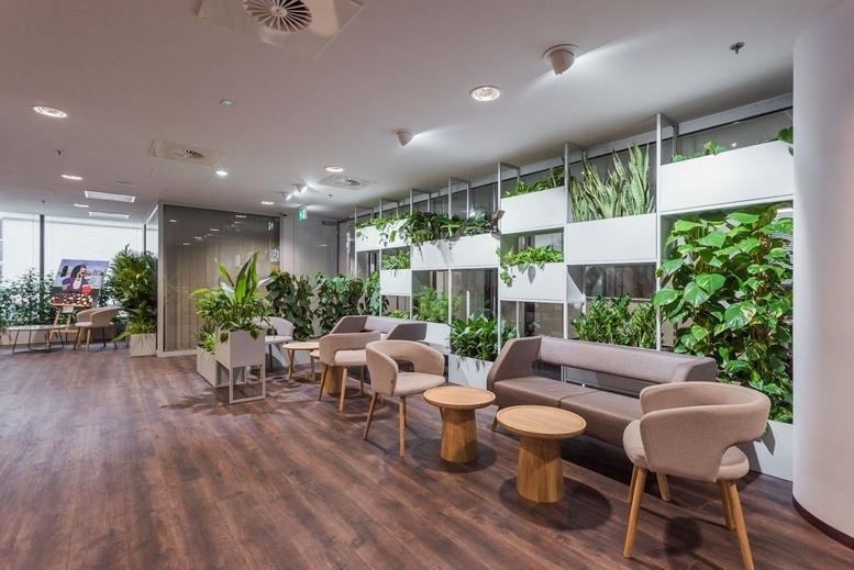 Spacious communal lounge at Al. Jana Pawła II 22 featuring wood floors and lush green living walls.
