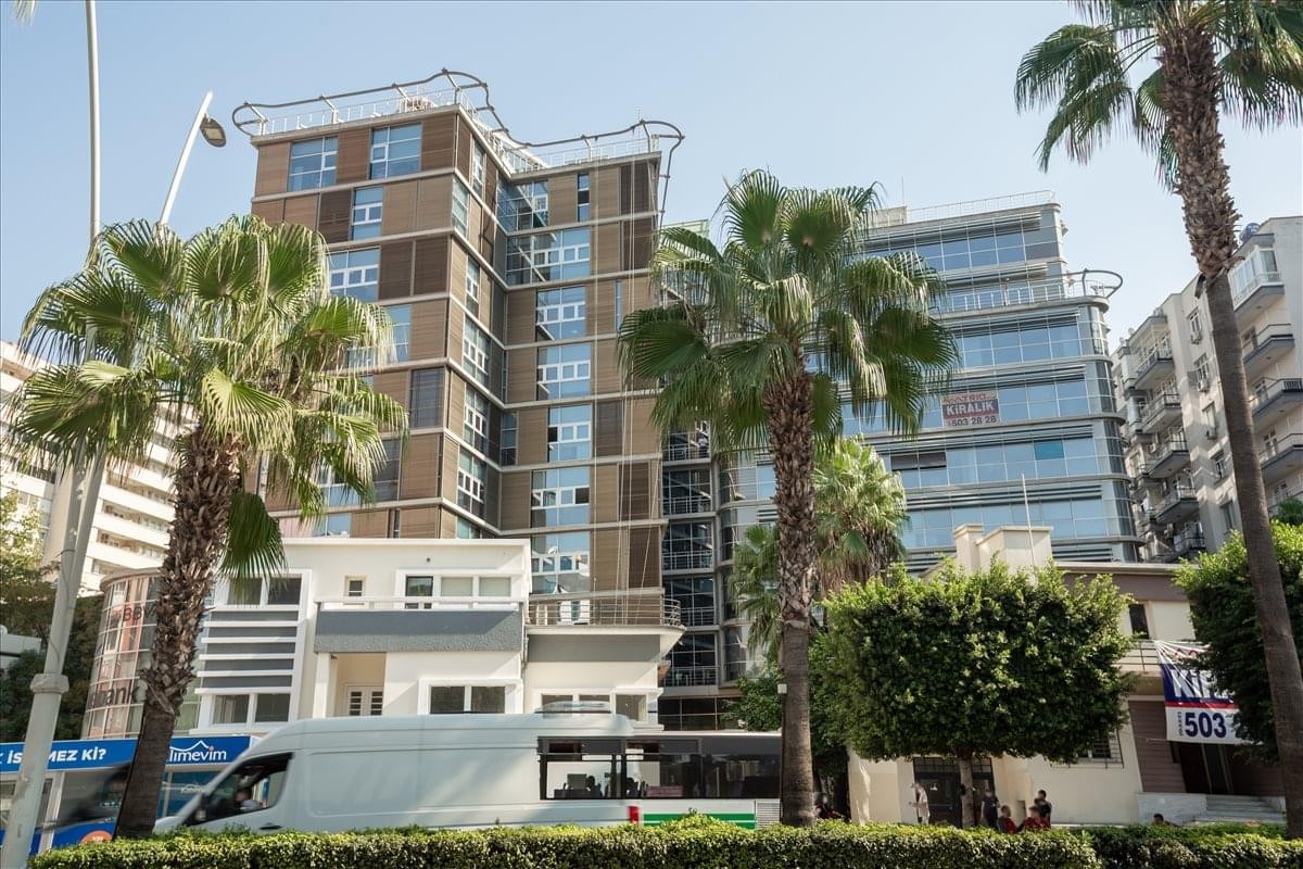 Exterior view of the multi-story Mimar Semih Rustem Is Merkezi building behind palm trees.