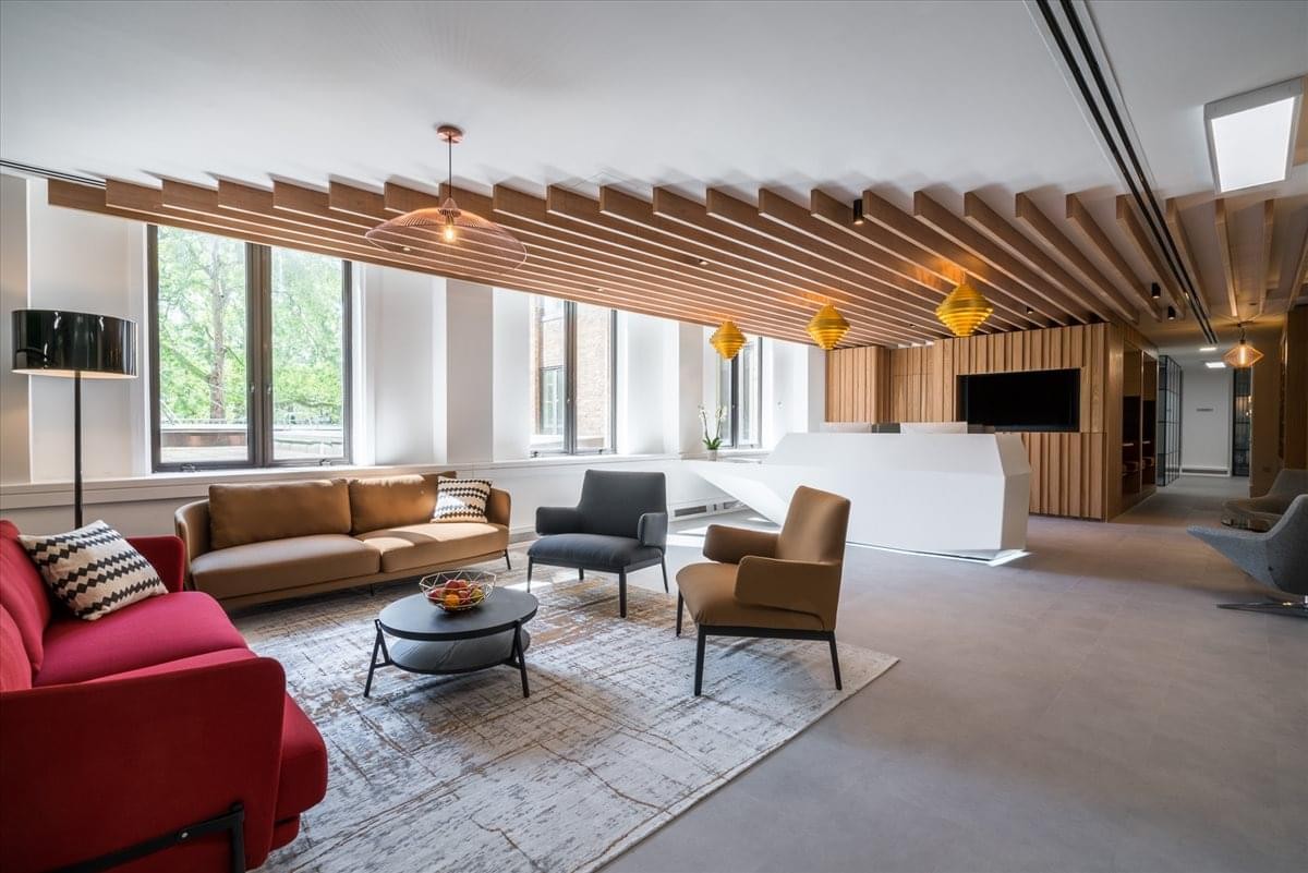 Sleek lounge at Berkeley Square House with a red sofa and architectural ceiling slats.