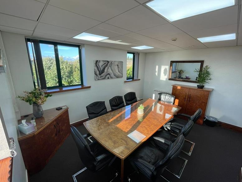 Spacious boardroom featuring a polished wood table, black leather chairs, and large windows.