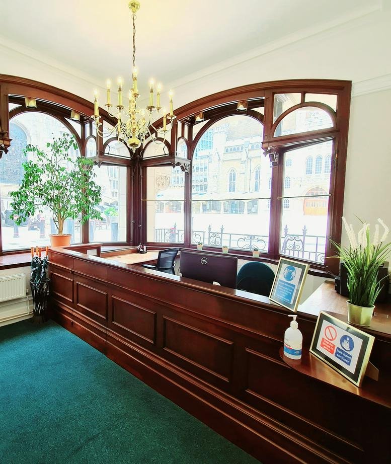 Grand wooden reception desk with arched window frames and a classic chandelier.
