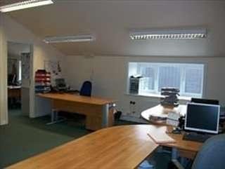 Open-plan office at Briar Rhydding House with wooden desks, blue chairs, and bright fluorescent lighting.