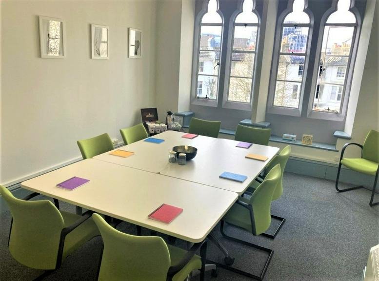 Meeting room at Brighton Forum with a large modular table, green chairs, and arched gothic windows.