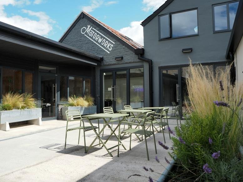 Exterior view of the dark grey Motorworks building with an outdoor seating area and greenery.