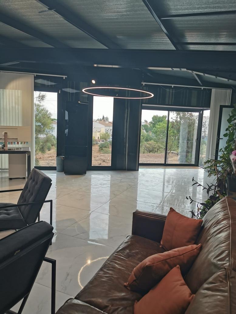 Spacious communal lounge at Calle Crianza 15 with leather sofa, orange pillows, and marble-style flooring.