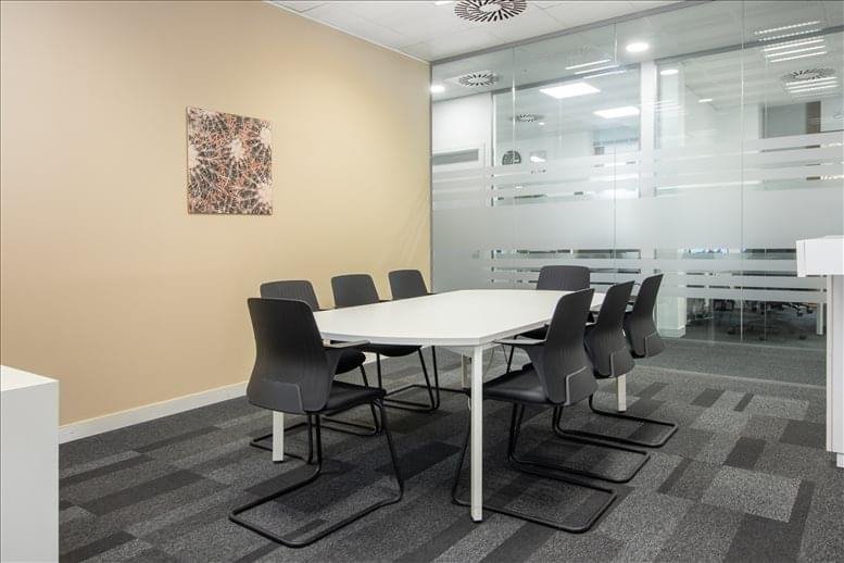 Professional boardroom with a white table, grey chairs, and a frosted glass wall.