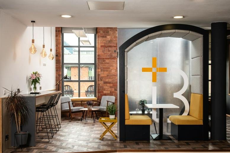 Open-plan coworking lounge with a breakfast bar, yellow booths, and large windows.