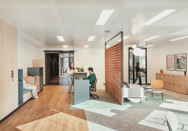 Open workspace featuring a brick-textured room divider and a mix of timber and carpeted flooring.