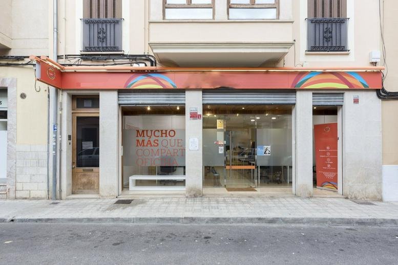 Exterior entrance and storefront of Carrer del Bisbe Maura 39 with large glass windows and red signage.