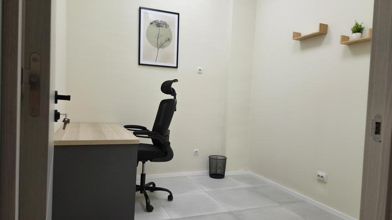 Bright private office room with a desk, ergonomic chair, and wall shelving.