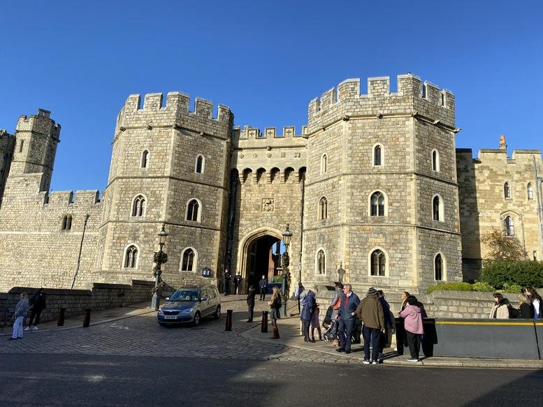 Exterior view of a historic stone castle gatehouse with crenellated towers under a blue sky.