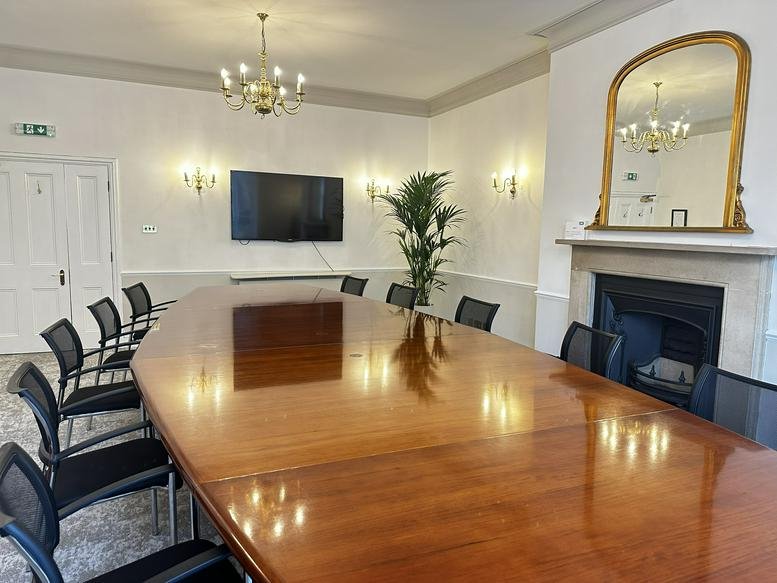 Grand boardroom with a long polished wood table, fireplace, and ornate gold mirror.