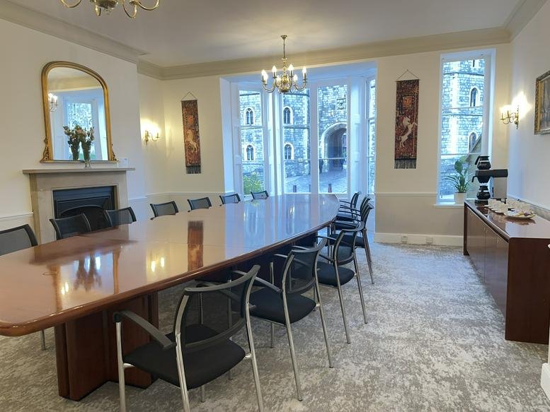 Grand meeting room with a large oval table, mesh chairs, and views of a stone courtyard.