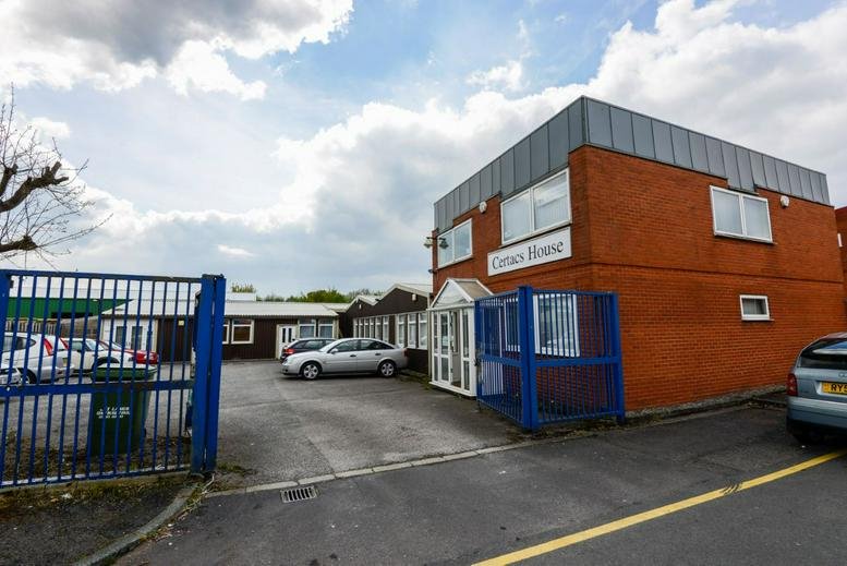 Exterior view of Certacs House, a two-story red brick office building with a paved parking area.