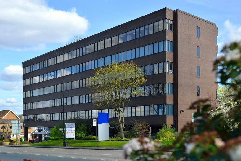Wide exterior shot of the multi-story brown brick office building under a blue sky.