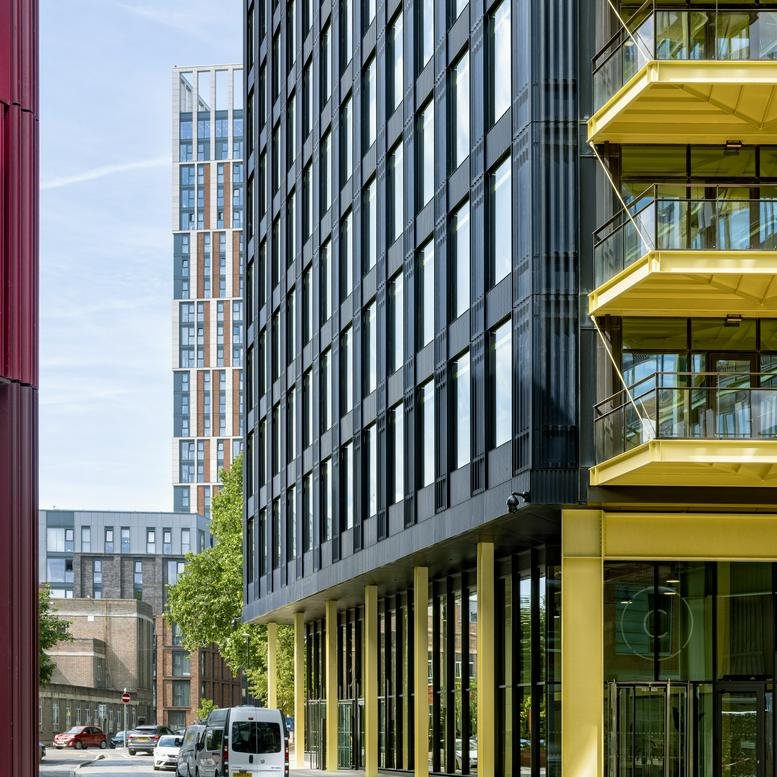 Exterior view of the dark-paneled facade and yellow structural beams at Assembly C, Cheese Lane.