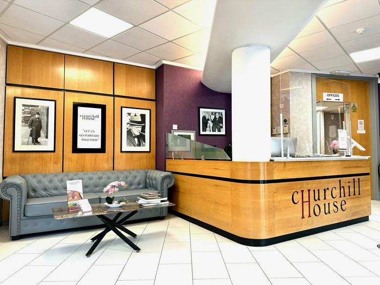 Modern reception area with a wood-paneled desk, purple feature wall, and grey tufted sofa.