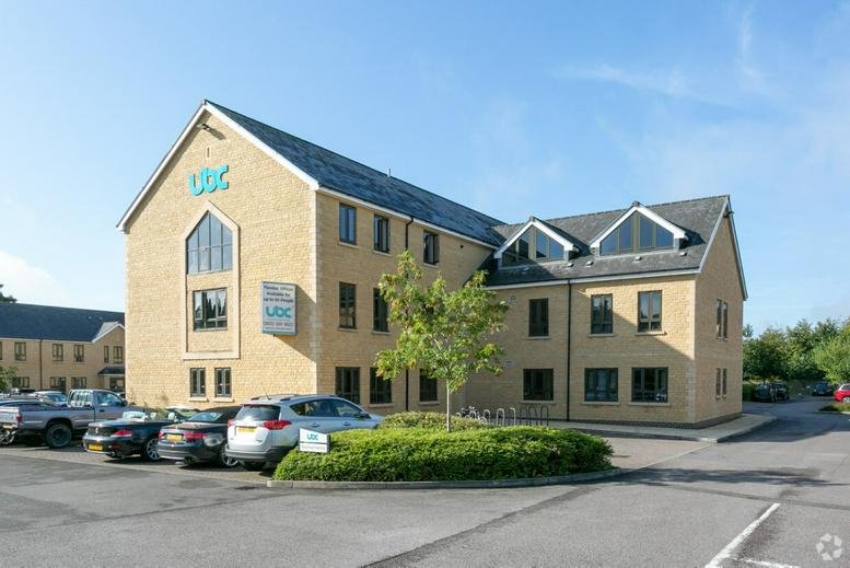 Exterior view of the stone-clad Cirencester Office Park building with parking and greenery.