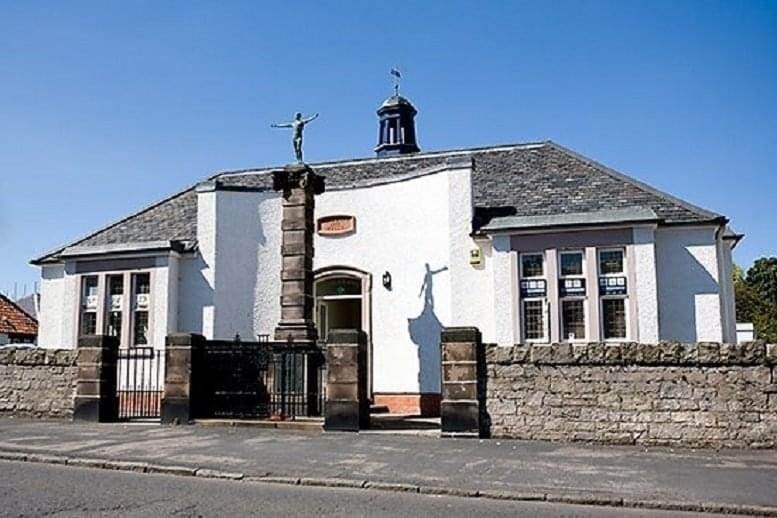 Exterior view of Cockburn Halls, George Street, Ormiston, East Lothian, Scotland featuring a statue and stone wall.