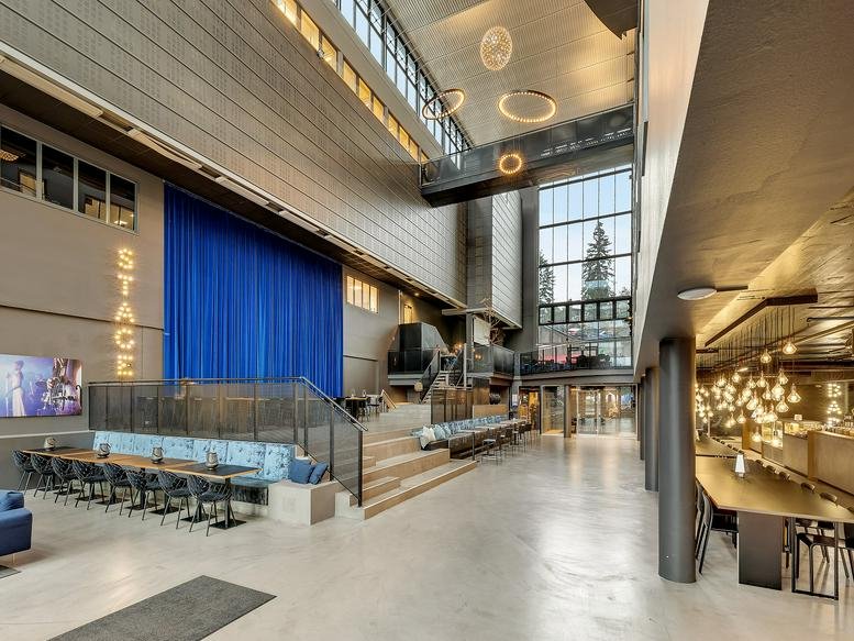 Grand lobby at Drammensveien 211 with a blue stage curtain, high ceilings, and tiered wooden seating.