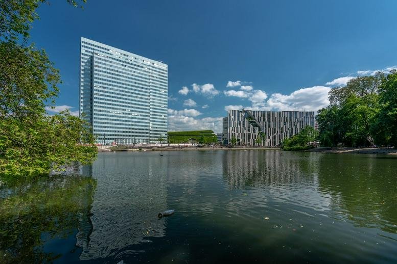 Exterior view of the iconic Dreischeibenhaus 1 skyscraper overlooking a serene lake and park.