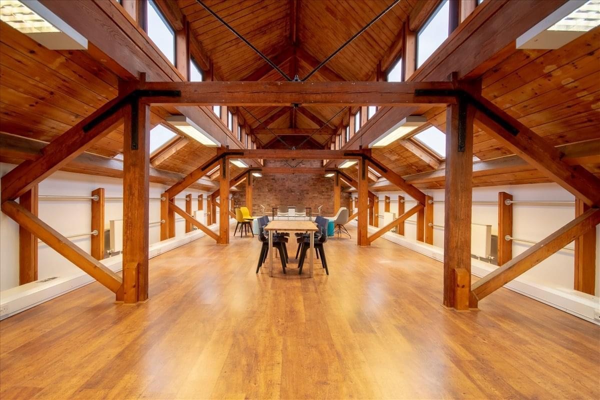 Large open-plan coworking space under a vaulted timber-beamed roof.