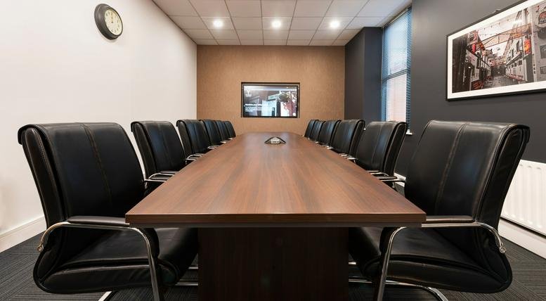 Spacious boardroom featuring a long wooden table and black leather executive chairs.