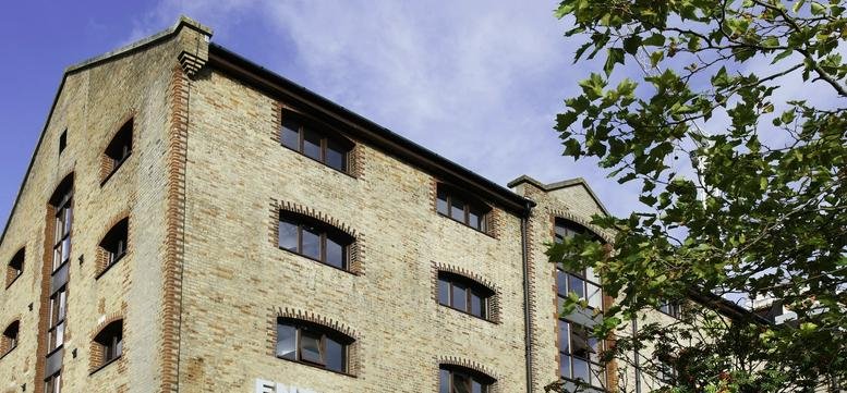 Exterior brick facade of Enterprise House, Ocean Village with large arched windows and a nearby tree.