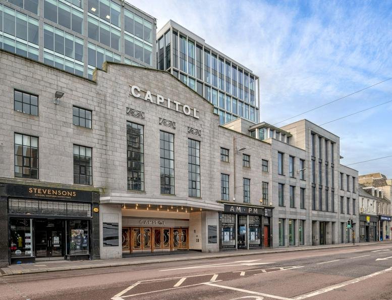 Wide view of a street-level stone building with the Capitol sign and glass office tower above.
