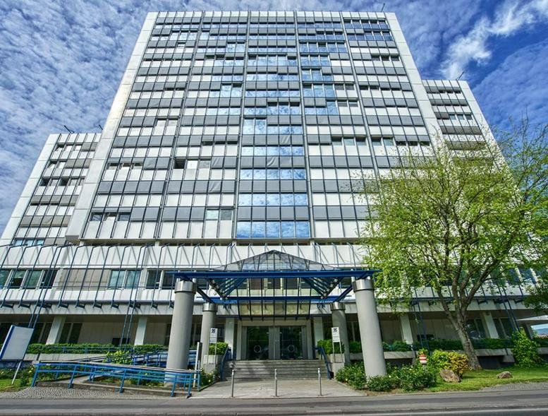 Low-angle exterior view of the multi-story First Choice Business Center Wiesbaden building with blue sky.