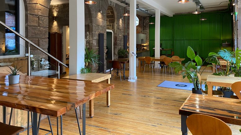 Wide open-plan workspace featuring wooden tables, potted plants, and stone archways.